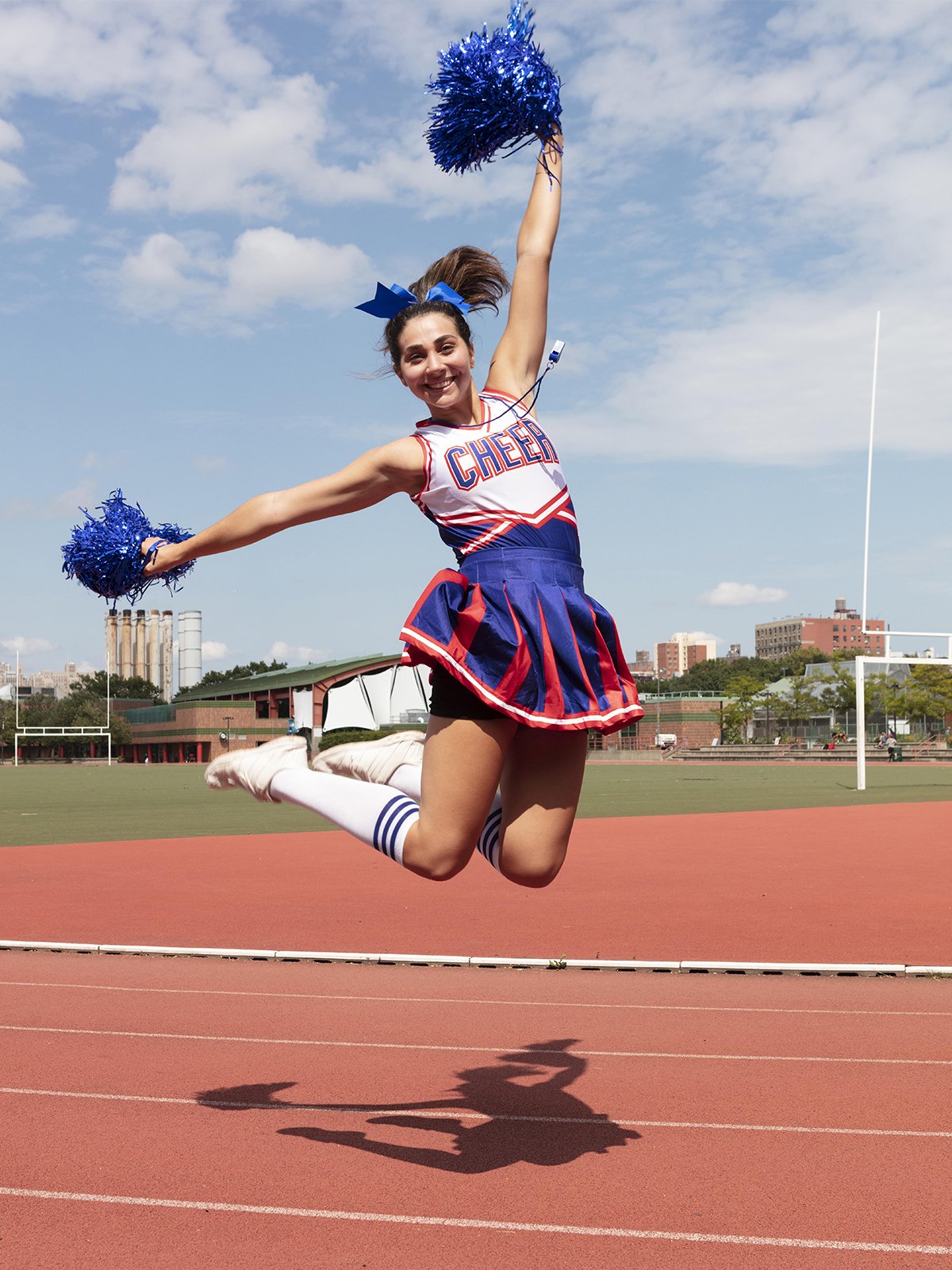 Cheerleader sautant sur un terrain de sport américain, skyline en arrière-plan
