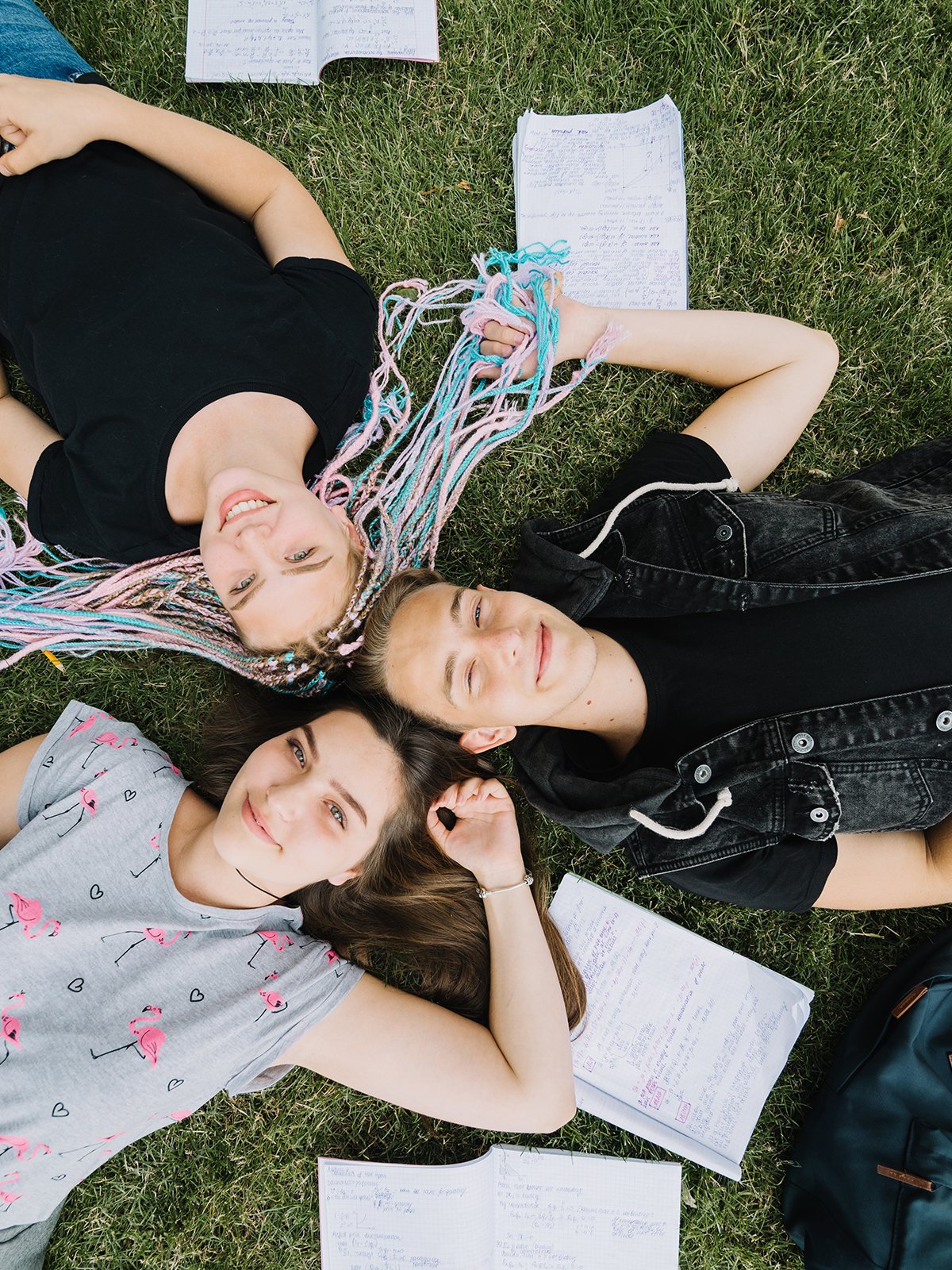 Trois adolescents allongés dans l'herbe avec leurs cahiers, souriants